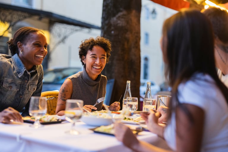 Group of cheerful young multi ethnic female friends enjoying dinner together, laughing and talking at an outdoor restaurant