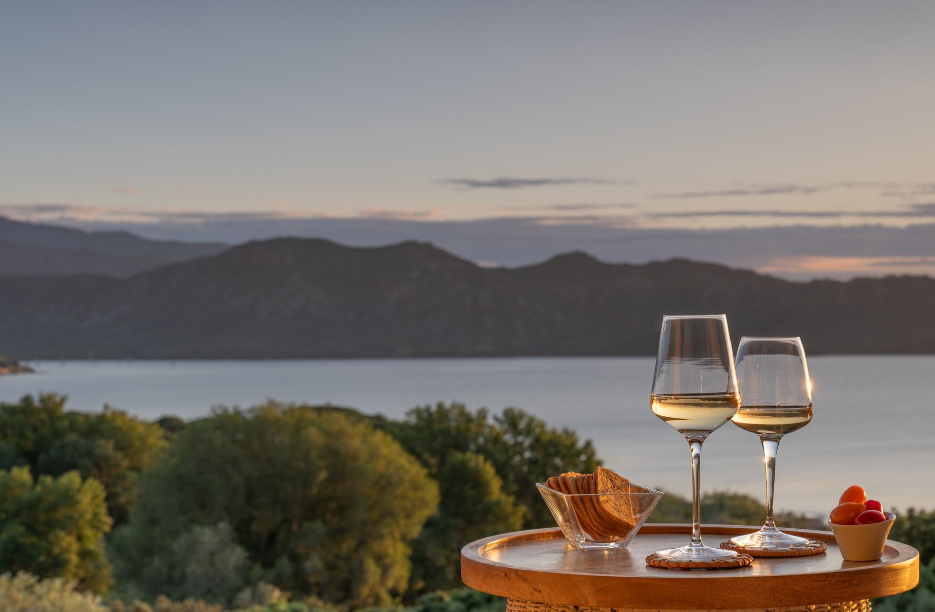 A wooden table with snacks and two wineglasses against a beautiful scenic backdrop