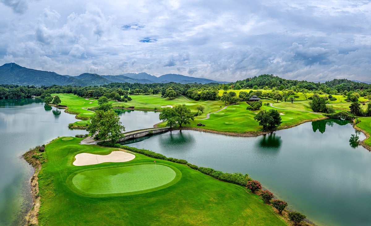 Scenic golf hole featuring a small bridge set against a backdrop of mountains dotted with wind turbines