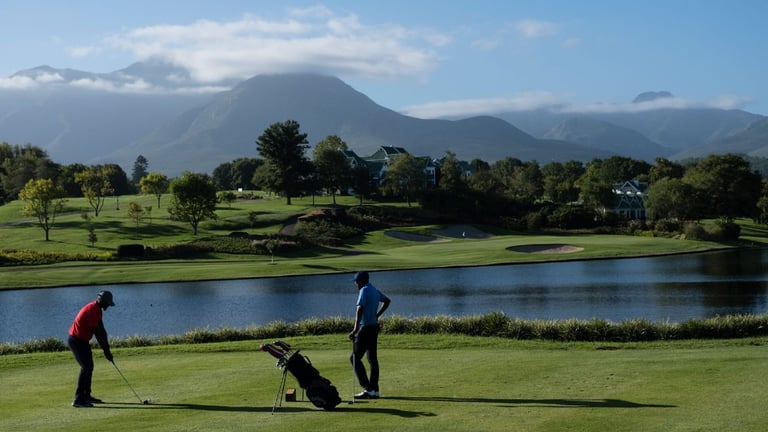 Golfers on a scenic course near a lake with mountains