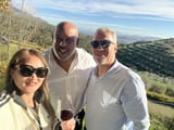 Three people smiling at camera holding wine glasses with rolling vineyard hills in background