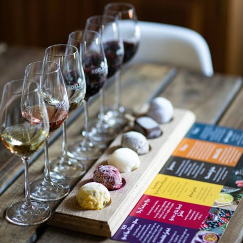 Wine tasting setup with five glasses progressing from white to red wine, paired with colorful truffles