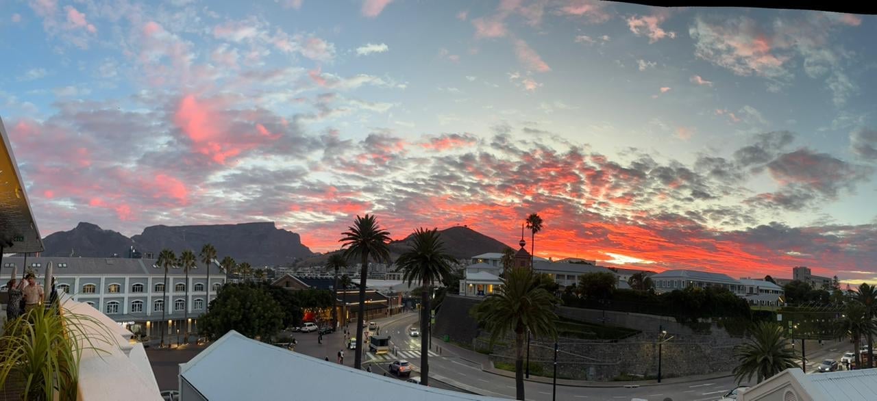 Sunset over Cape Town with Table Mountain, palm trees, and a colorful sky reflecting on rooftops